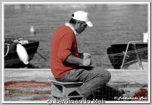 A fisherman patiently repairing his fishing nets. by Ferdinando Meli 